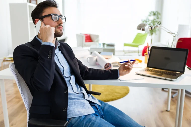 Homme en costume et lunettes, détendu, en pleine conversation téléphonique dans un bureau moderne.